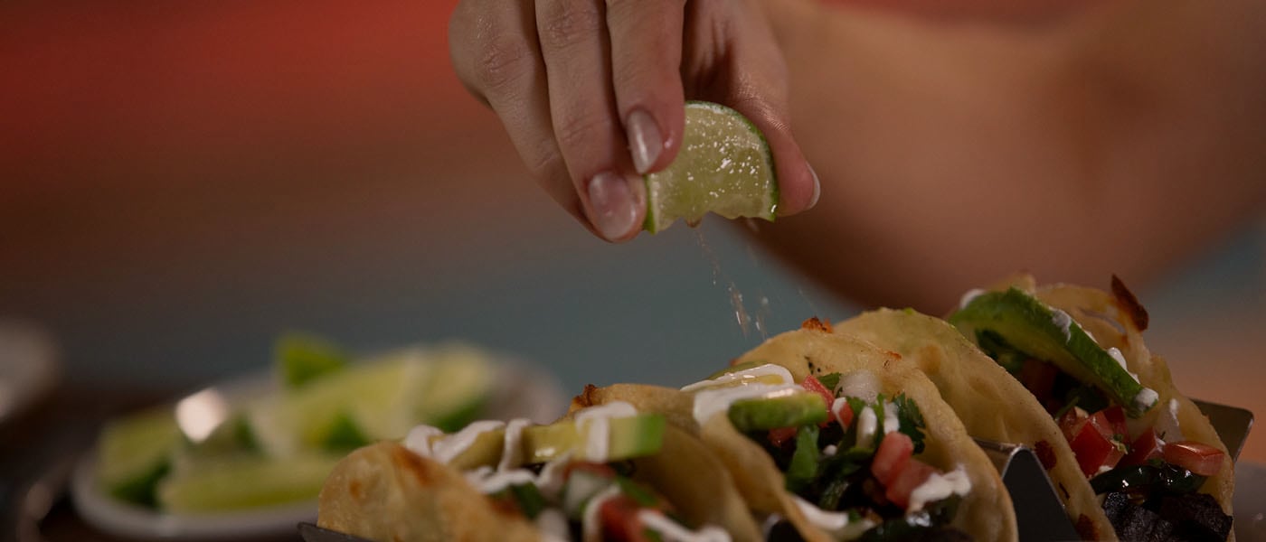 lime being squeezed over three street tacos