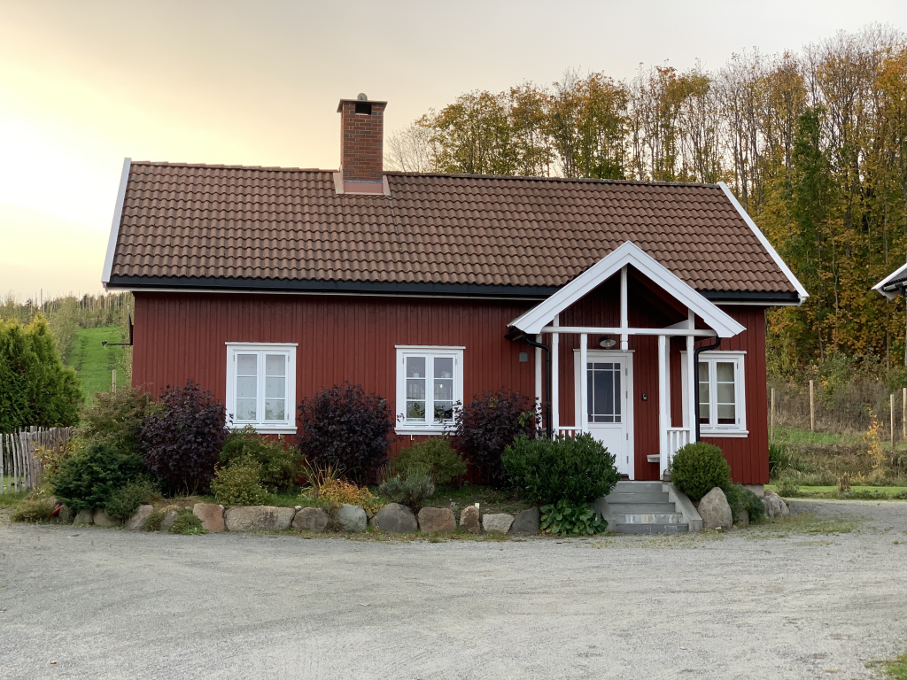 Bryggerhuset har et koselig inngangsparti og utgang bak som vender mot hagen. I bakgrunnen kan du skimte nabogårdens økologiske eple- og pæreranker.