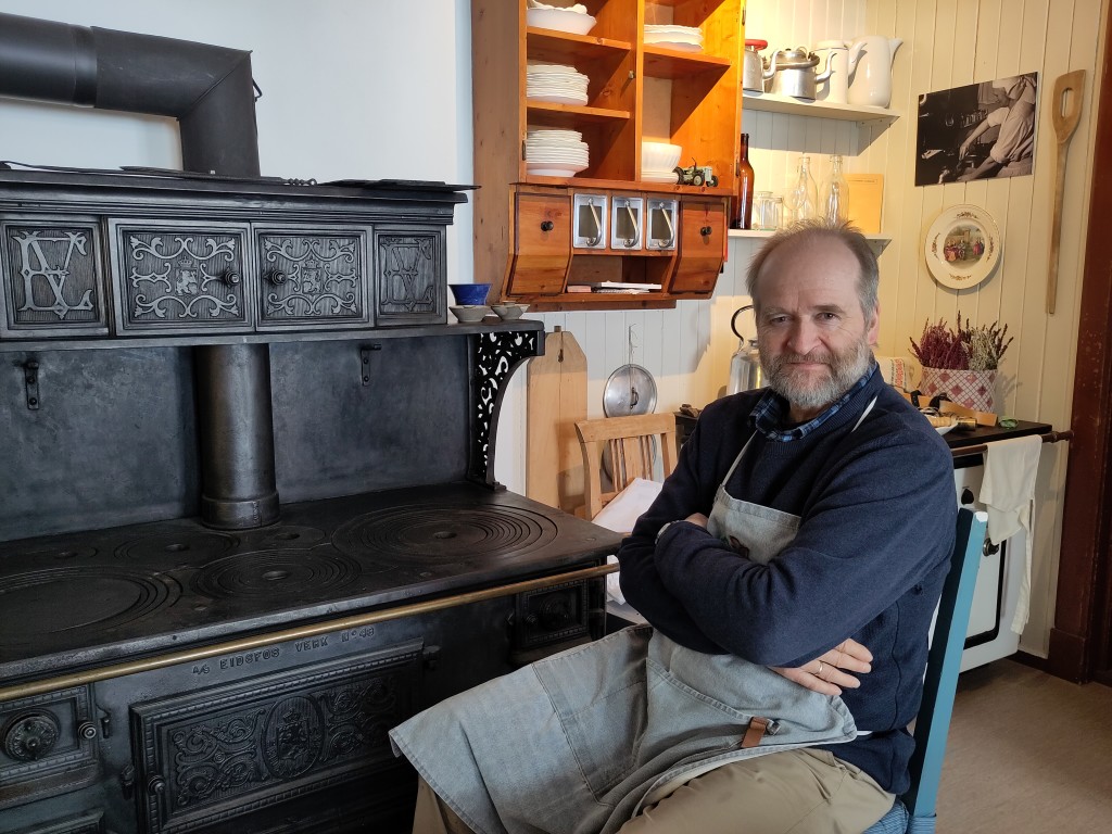 Lars Harald tar en pause ved den gamle kjøkkenovnen på gamlekjøkkenet. Når vi fyrer der er det godt å sitte der og kvile litt innimellom serveringa på pensjonatet.