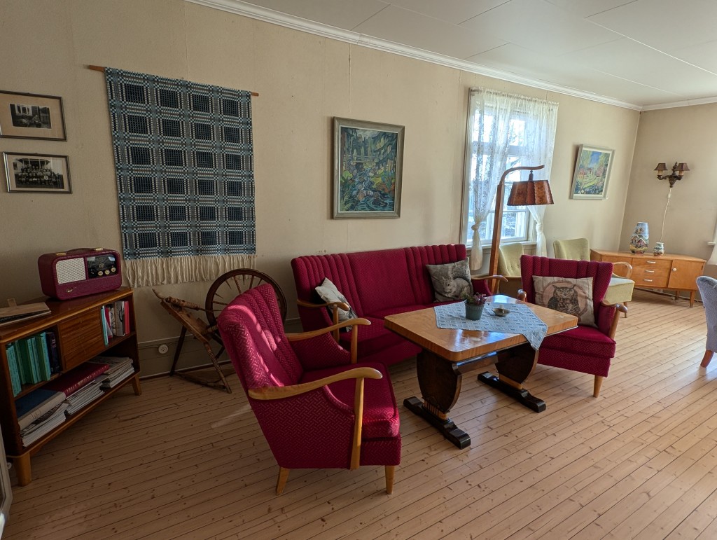 Salongen i pensjonatet. Flere av maleriene er malt av kunstneren Kalla Skrøvset da hun bodde her på 1950 tallet. Mange av bildene ellers i pensjonatet er malt av lokale kunstnere og er til salgs. Her kan du låne bøker og magasiner og kose deg i godstolen eller ta en trudelutt på det gamle Granumspianoet. Fotograf: Marianne Konow