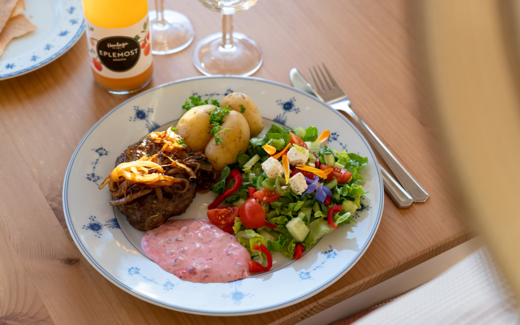 Vi serverer hjortekarbonader fra Setton Gård - en nabogård med hjorteoppdrett og eget lokalmatutsalg. Her med lokale poteter, tyttebærrømme, råkostsalat og hjemmebakt flatbrød. Det smaker forfriskende med eplemost fra epler dyrket ved Randsfjorden.