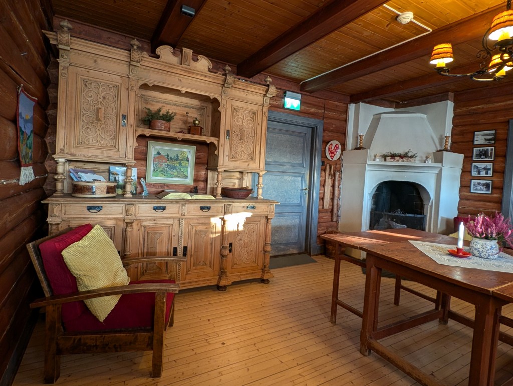 Peisestua med peis og tømmervegger. Flere av møblene her er snekret på gårdens snekkerverksted i 1930 åra.