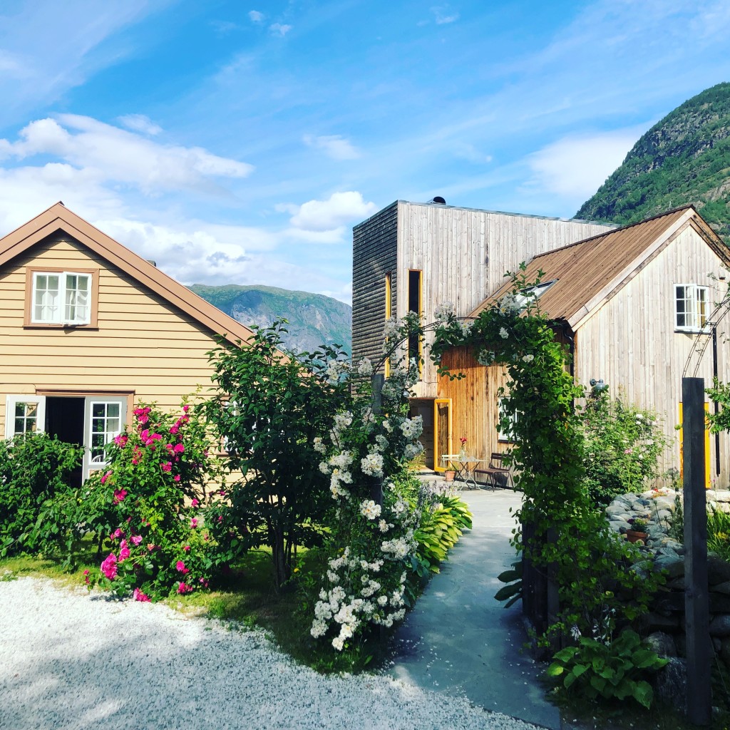Gårdsplassen med en av våre blomstrende rosebuer, med "Geitefjøsen"(t.h) og Fiskerhuset(t.v) i bakgrunnen. 
Eng: Our welcoming garden, a beautiful arch of roses, with our historic fishermanscabin to the left and our "Goat barn" to the right.