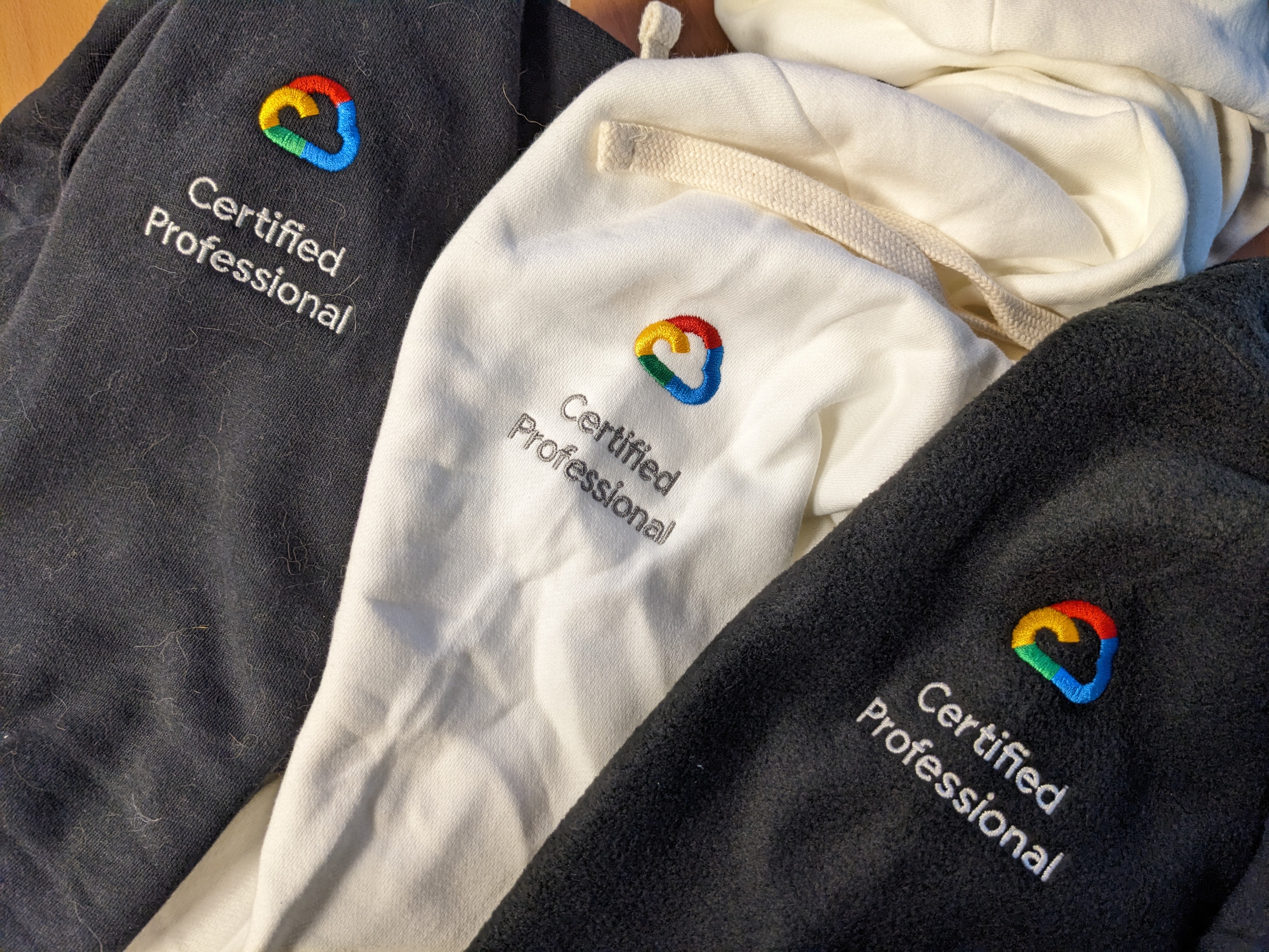 A collection of three hoodies and jackets - two black and one white - all featuring the embroidered Google Cloud "Certified Professional" logo.