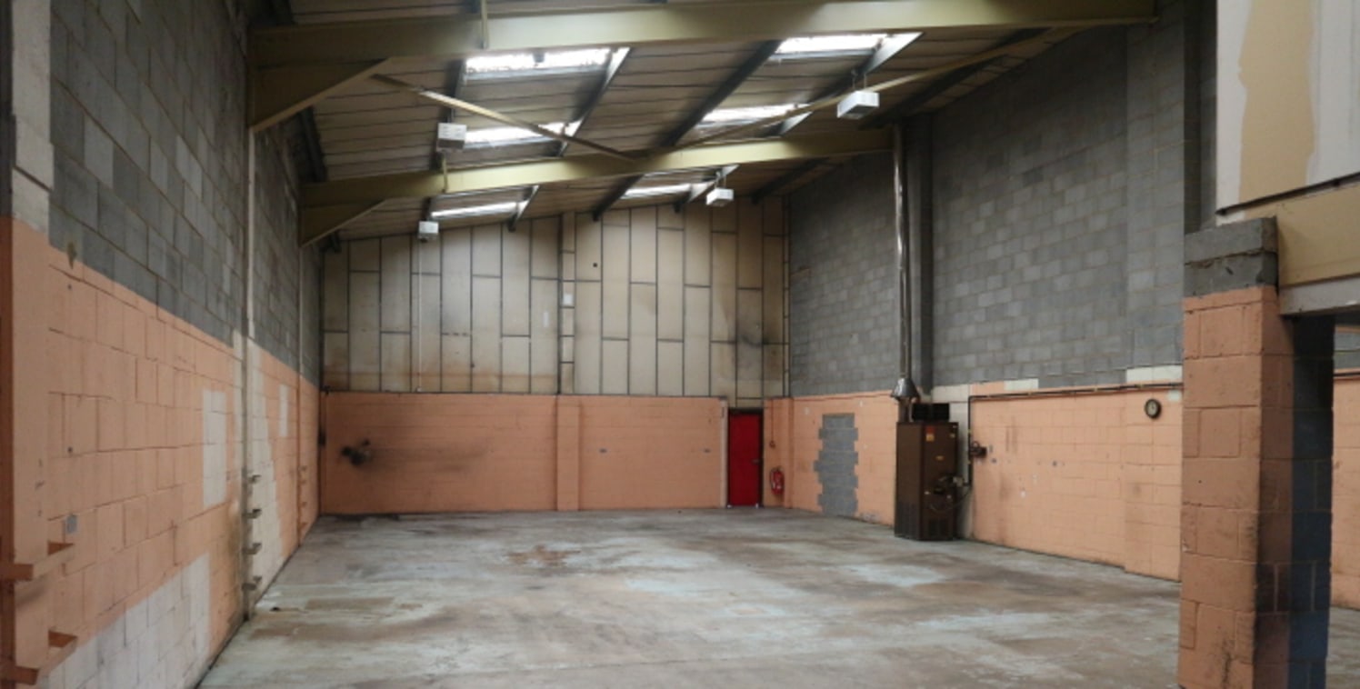 A mid-terrace industrial / warehouse unit of traditional steel portal frame construction under a pitched roof incorporating translucent roof panels.