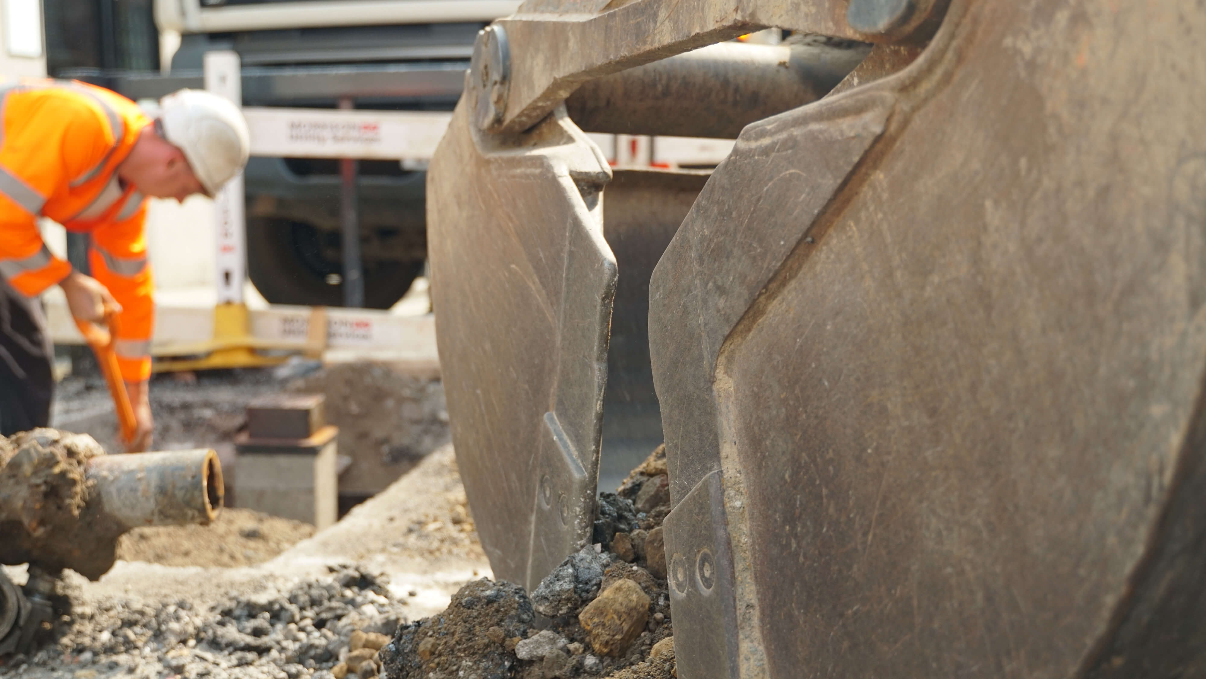 Roadworker in high-visability jacket and white hard hat  laying water pipes