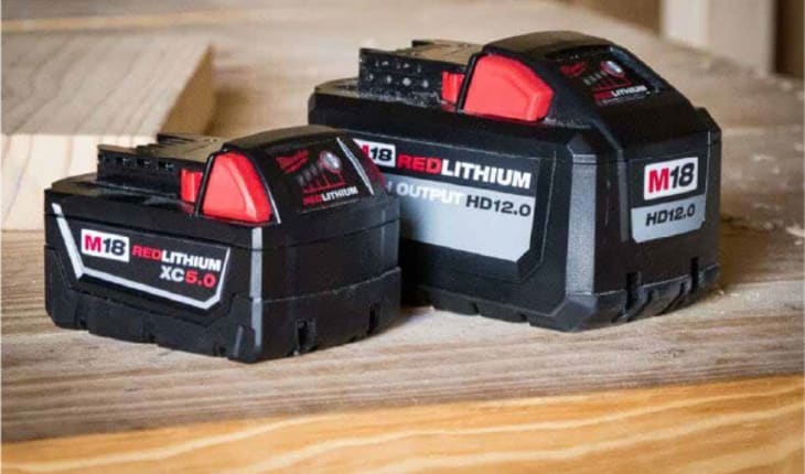 Power Tool Accessories: Two Milwaukee M18 Red Lithium batteries sit side-by-side on a sawdust-covered worktable.