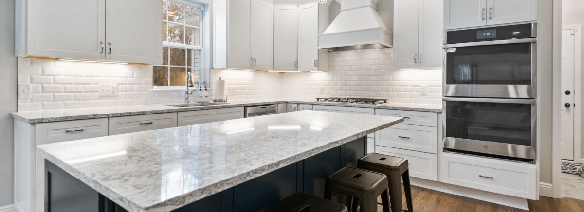 Elegant shaker kitchen with double wall ovens, concave hood, and white cabinetry.