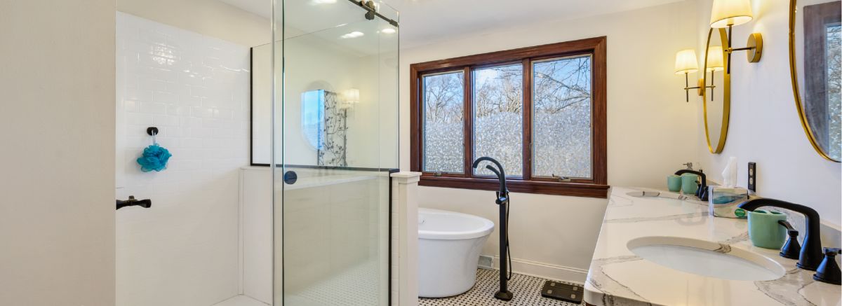 The retro bathroom with a shower with black trim, the freestanding tub, large windows in the background, and a Cambria vanity top.