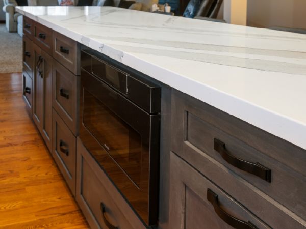 A close up of the kitchen island white brown cabinets, Cambria countertops, and a built-in microwave.