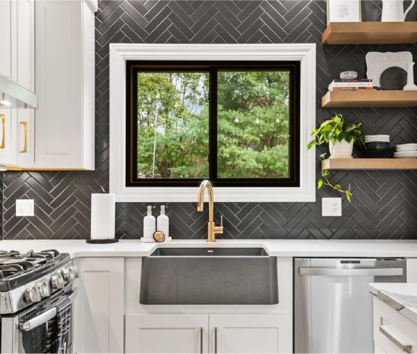 The black herringbone backsplash contrasted against white shaker cabinets with gold hardware. 