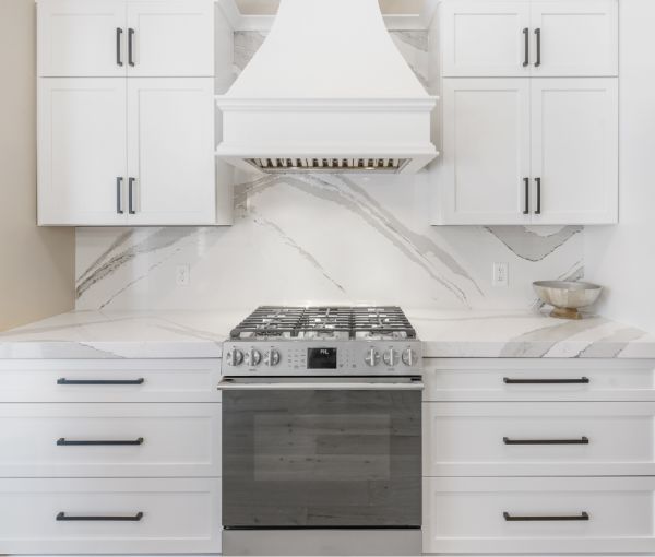 The concave wood hood over the stainless stove, the full-height backsplash, and white cabinets.