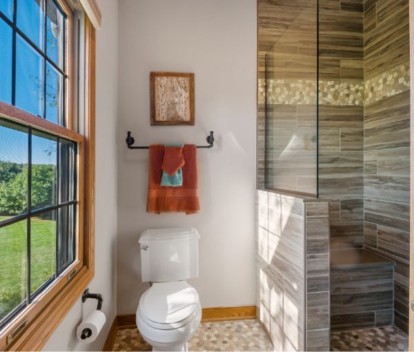 The white toilet and shower with wood-like tile and pebbled trim.