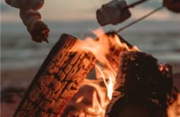 People roast marshmallows over a flaming wood fire pit