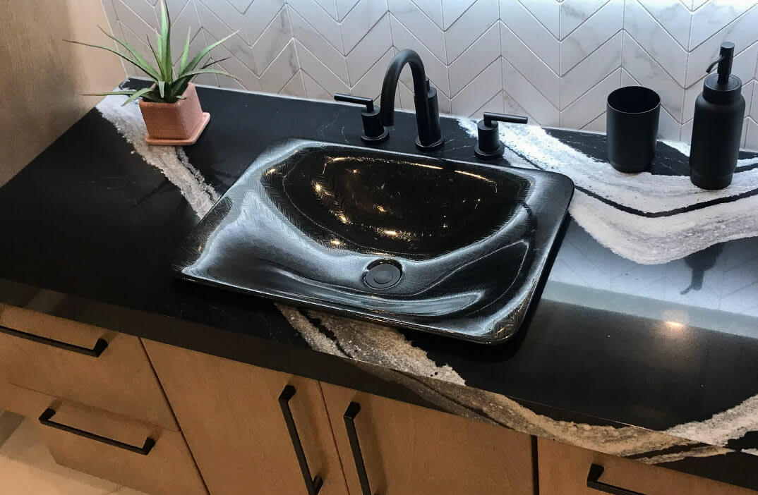 Black & white marbled Cambria bathroom countertop with a black sink, faucet, toothbrush holder & soap dispenser.