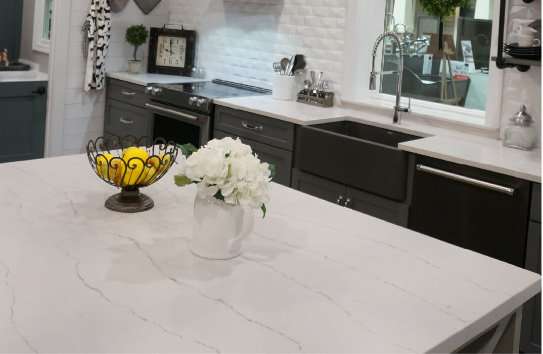 White Cambria quartz countertop on a kitchen island with a white vase of flowers and a metallic bowl with lemons.
