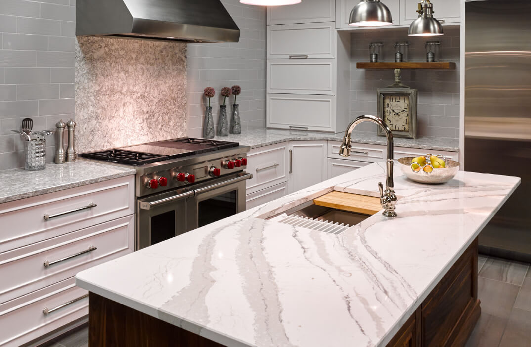 Kitchen with gray & white speckled Cambria countertops and an island with Cambria gray & white marbled countertops.