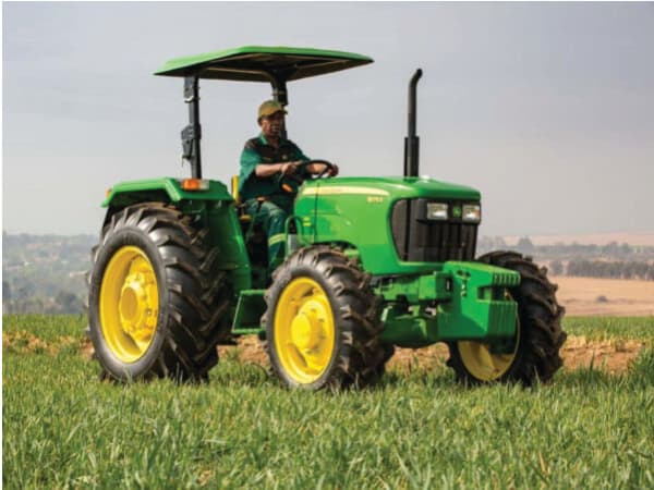 A man in John Deere clothing riding a John Deere tractor through a grass field.