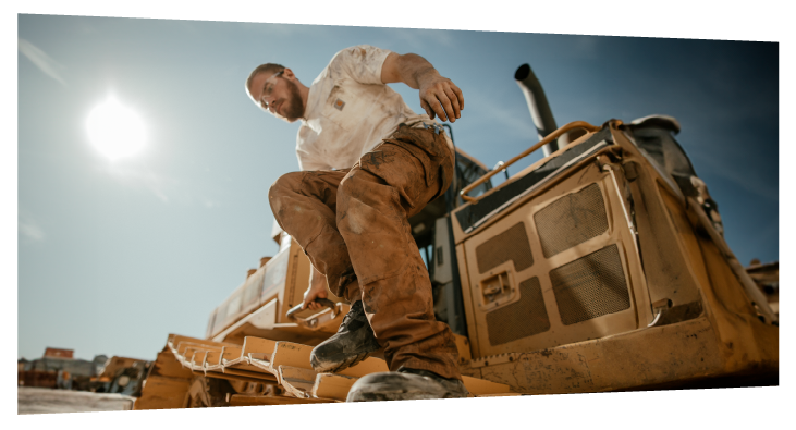 A man in Carhartt workwear stepping down from a tractor.