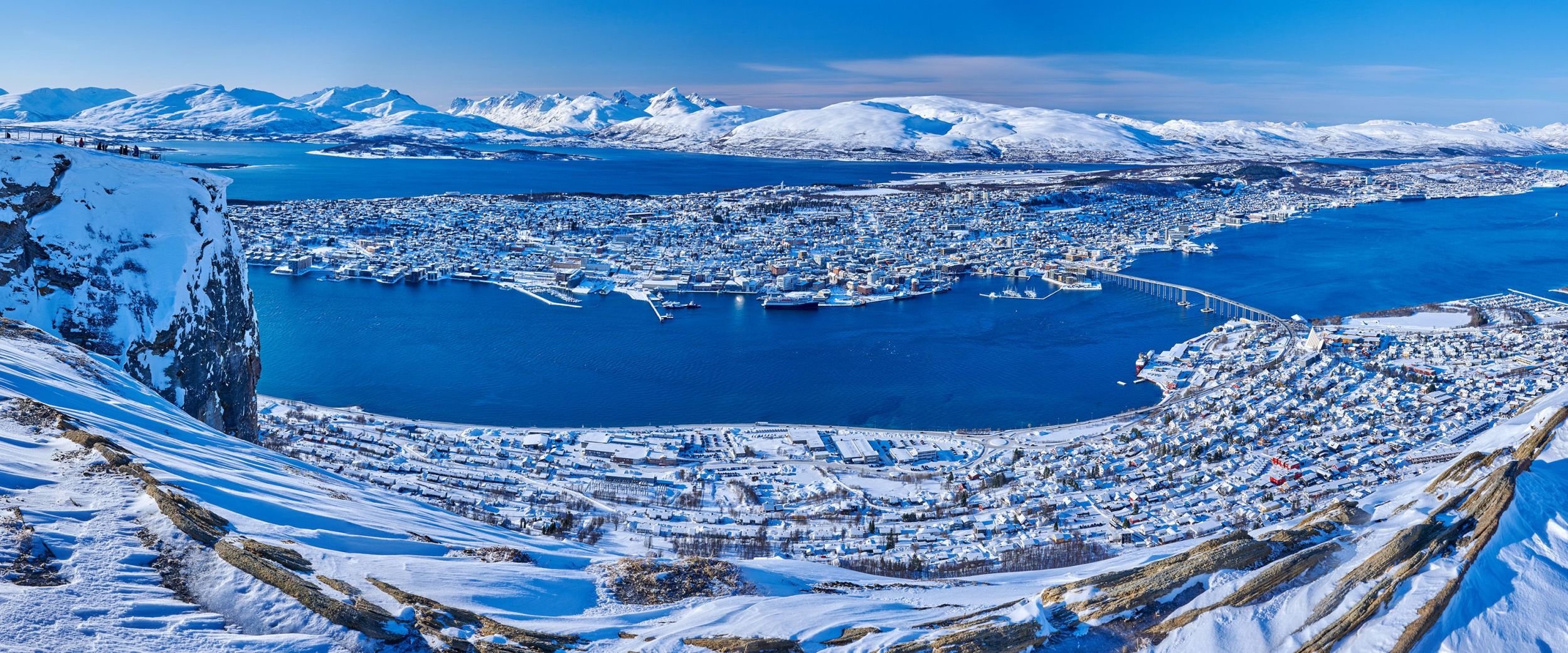 Panoramic vinter view of Tromsø from the Cable Car on a clear day. Snow-covered mountains, fjords, and islands surround the city stretching across the peninsula.