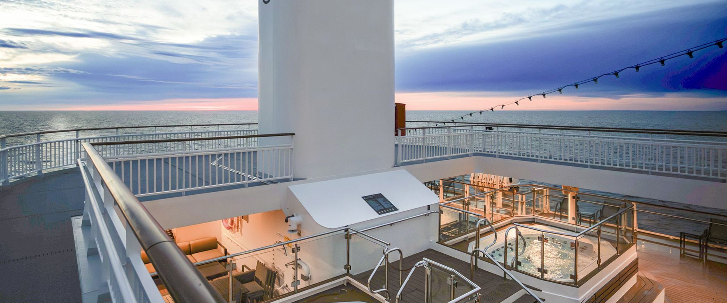Two modern jacuzzis on the deck of a cruise ship under a glowing blue evening sky, with a wide view of the ocean and a dramatic sunset on the horizon. A calm and exclusive atmosphere at sea.