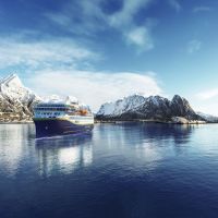 Havila ship on a calm sea with the Lofoten mountains in the background.