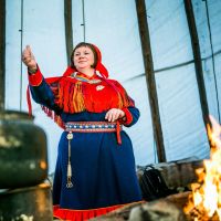 Sami woman cooking on a campfire in the lavvo, wearing a traditional costume. Photo: Christian Roth Christensen, Visitnorway.com