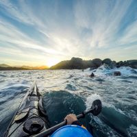 Kayak in the sea paddling  towards the mountain filled mainland with a sunset in the background.