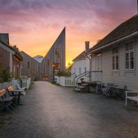 Street in Romsdalsmuseet with traditional houses and modern museum building in sunset.