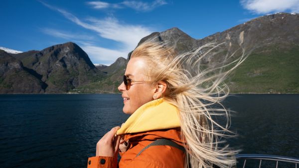 Traveler on deck wearing a jacket and scarf in windy fjord conditions.