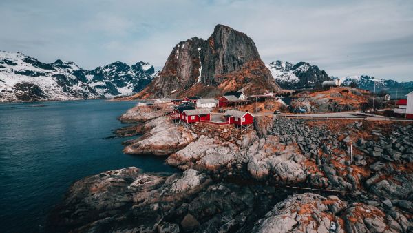 Red houses on rocky shoreline with majestic mountains in the background.