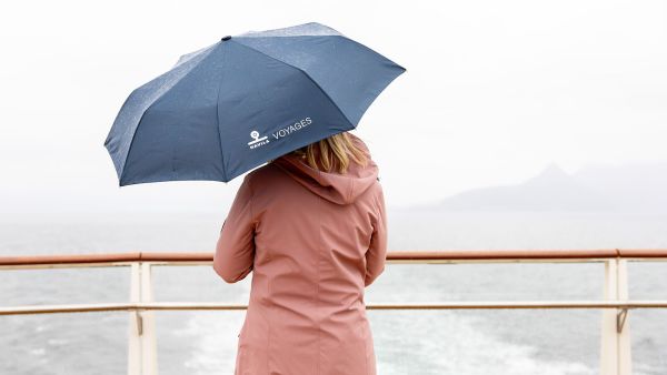 Person holding an umbrella on a ship deck in rainy weather.