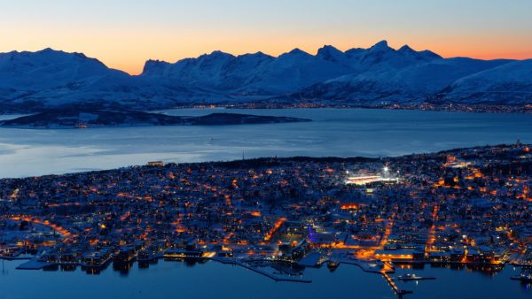 Downtown Tromsø seen by night and a fantastic orange blue city light scenery with a beautiful backdrop of mountains and orange to light blue heaven.