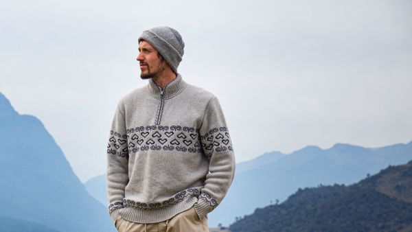 Person wearing a knit sweater and beanie in an open landscape with mountains in the background.