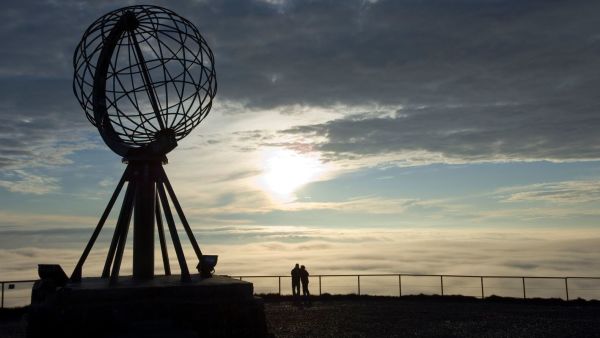 People watching the midnight sun next to the globe at the North Cape. Photo: Johan Wildhagen, visitnorway.com