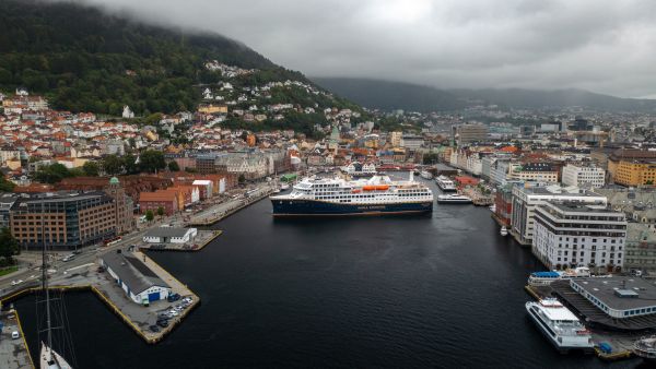 A Havila Voyages ship in Bergen, with the colourful Bryggen waterfront and houses climbing the mountainside behind the city.