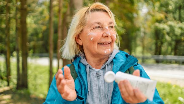 woman in a blue jacket applying sunscreen before hiking during summer