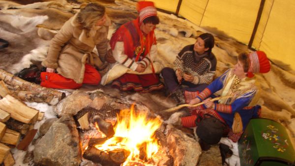 People around the campfire in a sami telt dressed in traditional sami costumes. Photo: Trym Ivar Bergsmo, nordnorge.com