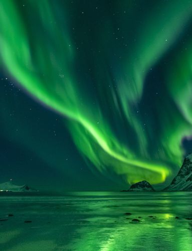 Northern lights over mountain and with reflection in the sea. 