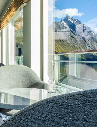 Comfortable lounge chairs facing panoramic windows with a view of fjords and snow-covered mountains from Havblikk Bar & Lounge on board Havila Voyages.