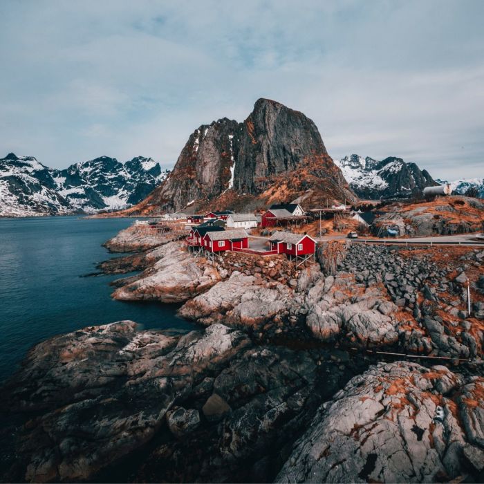 Red houses on rocky shoreline with majestic mountains in the background.