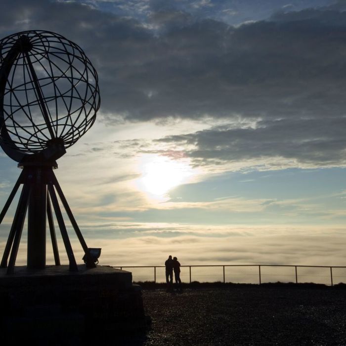 People watching the midnight sun next to the globe at the North Cape. Photo: Johan Wildhagen, visitnorway.com