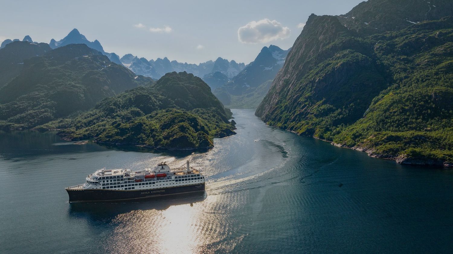 A ship gliding through a dramatic Norwegian fjord, surrounded by towering, green-clad mountains and mirrored waters under a bright, partly cloudy sky.