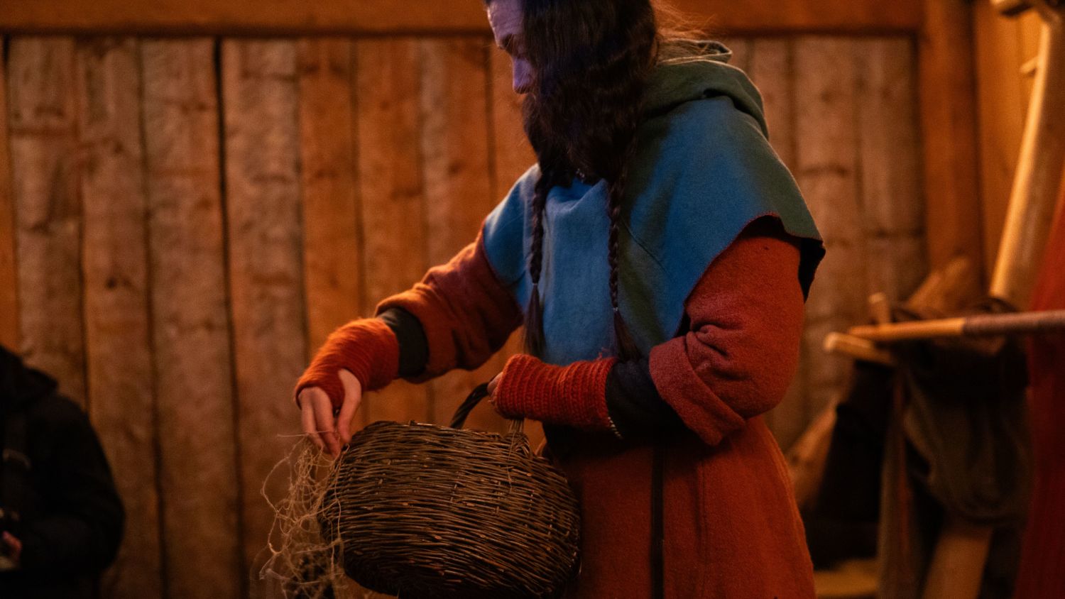 Person in traditional clothing demonstrating craft work inside a medieval-style wooden interior