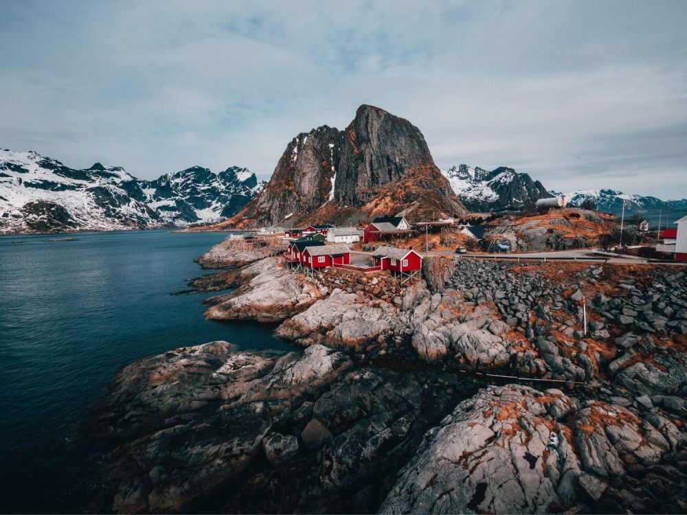 Red houses on rocky shoreline with majestic mountains in the background.