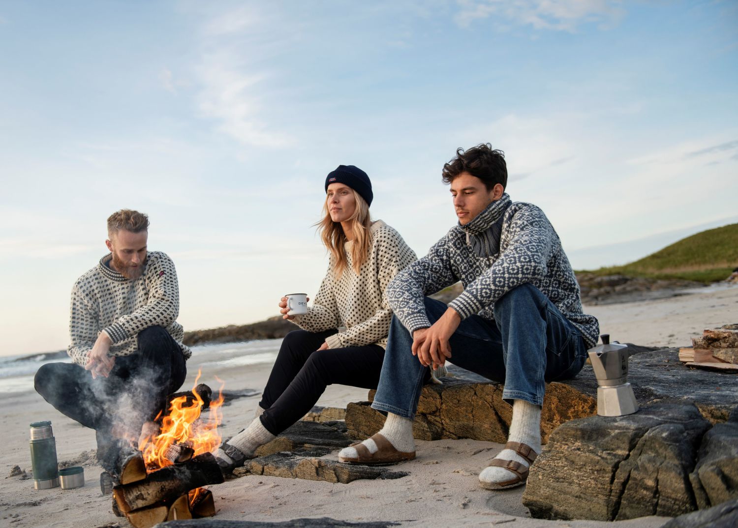 Young people at the beach with a bonfire, dressed in knitted sweaters. Photo: Devold.no