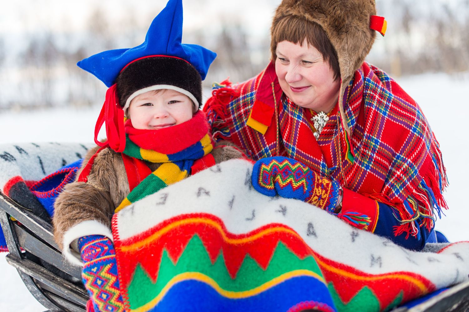 Sami child in a sled and a sami woman, both dressed in traditional costumes. Photo: Ørjan Bertelsen, nordnorge.com