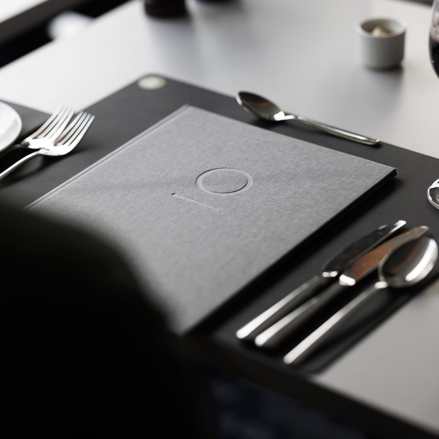 Table setting with cutlery and a grey menu folder on a dining table