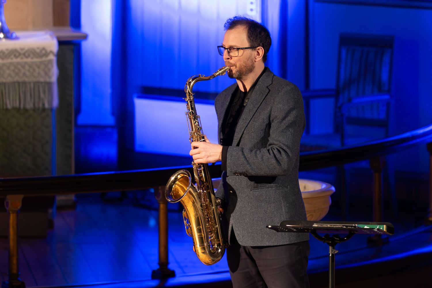 A saxophonist performing during a midnight concert inside Tromsø Cathedral, standing on stage under blue lighting with the instrument held close as he plays.