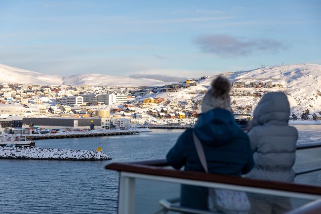 Guests arriving in Hammerfest with Havila Voyages, viewing the town from the ship’s deck as snow-covered hills and buildings line the harbor.